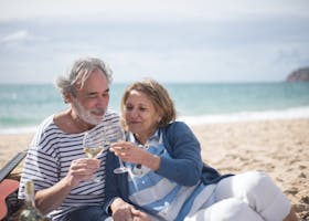 Happy senior couple enjoying a romantic moment with wine on a scenic beach in Portugal.